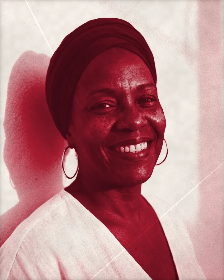 Portrait of a smiling woman in a deep red head wrap with big gold hoops, printed for the wall