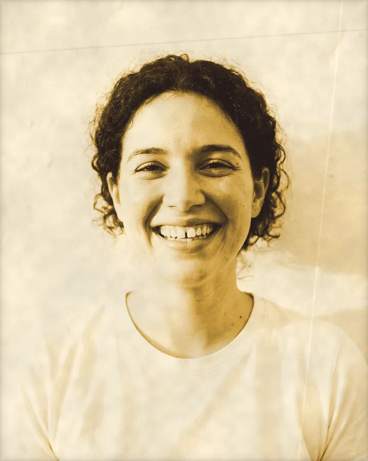 Portrait of a young woman with dark curly hair and a big gap-toothed grin, printed for the wall