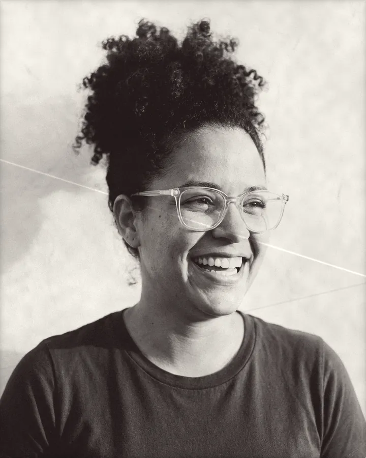 Portrait of a laughing woman with curly hair in a high puff and clear glasses, printed for the wall