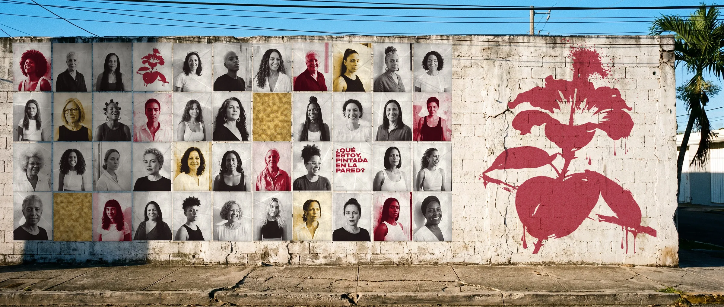 A long white block wall in Santurce covered with wheatpasted portraits of Puerto Rican women in black and white, Bija red and gold, a poster reading ¿Qué estoy, pintada en la pared?, and a huge red flor de maga sprayed at the right